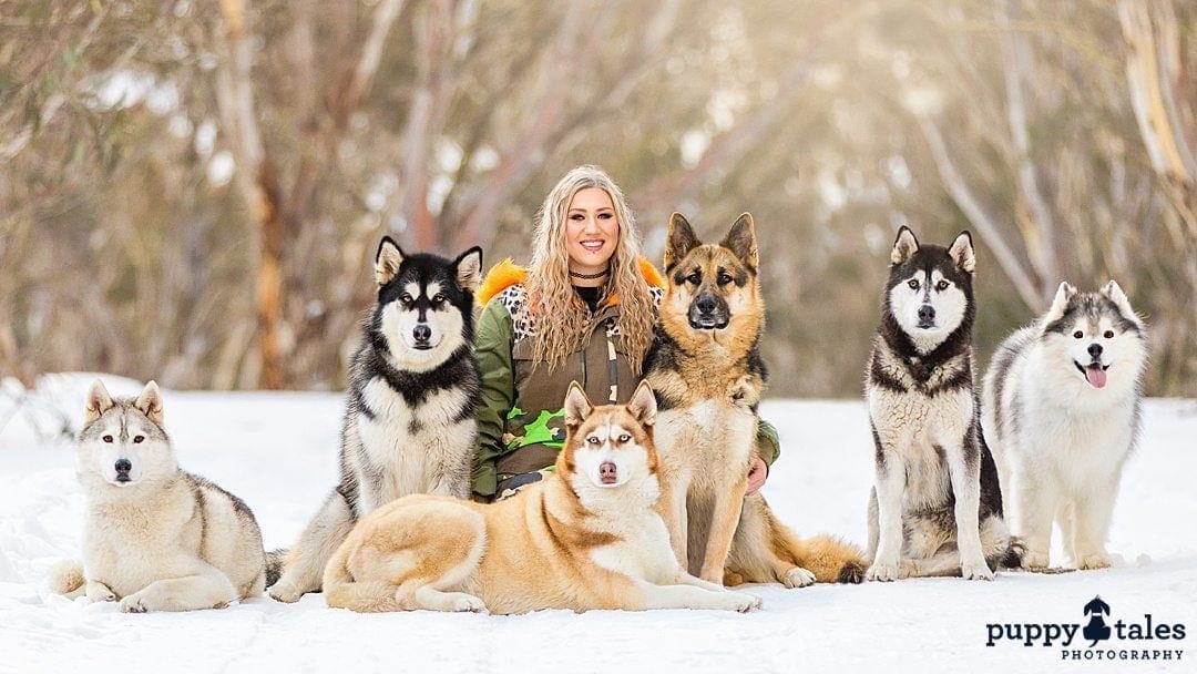 a woman posing for the camera with her six dogs