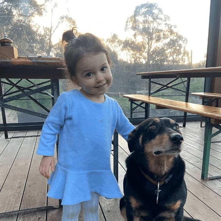 Little girl posing for the camera with a black dog in dog friendly cafe in Melbourne