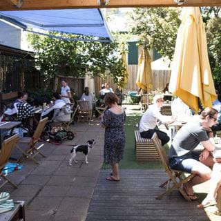 A lively and bustling outdoor view of a popular dog-friendly brunch spot in Melbourne, showcasing diners enjoying their food and soaking up the sun.