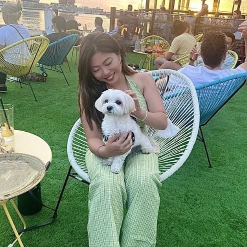 In a dog-friendly cafe in Melbourne, a woman and her small white dog enjoy the sunshine and the sights of the bustling city, with the dog sitting on her lap