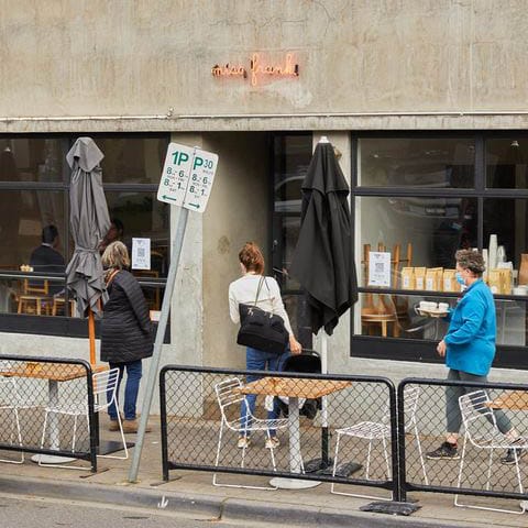 An outdoor view of a cozy pet-friendly cafe in Melbourne, where three people can be seen walking into the cafe, perhaps to dine with their furry friends.