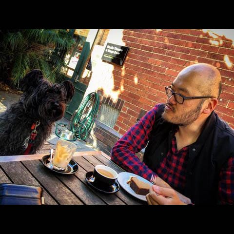 A dog-friendly cafe in Melbourne provides the perfect setting for a man and his furry friend to enjoy a delicious meal together. The pet owner is seen savoring a tasty dessert and freshly brewed coffee, with his dog comfortably seated in front of him.