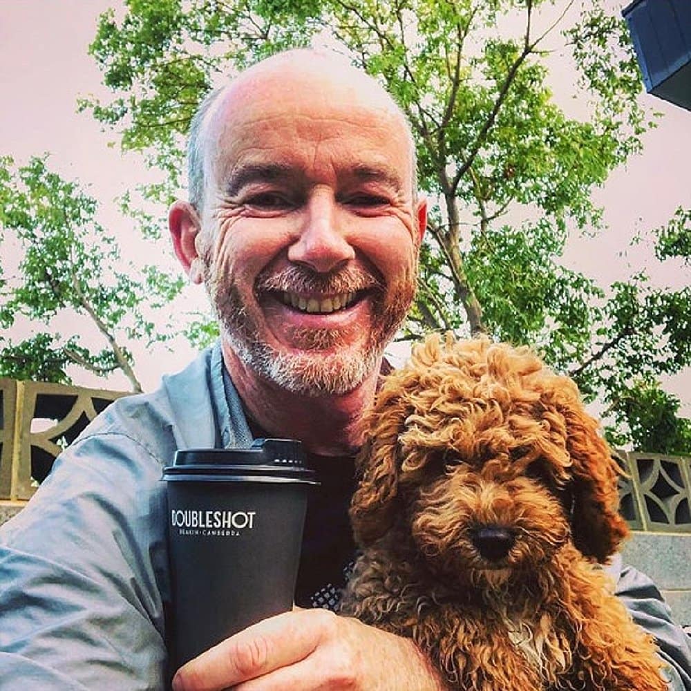 A man taking a selfie with his dog on his lap and his coffee in a dog friendly cafe called Doubleshot Deakin