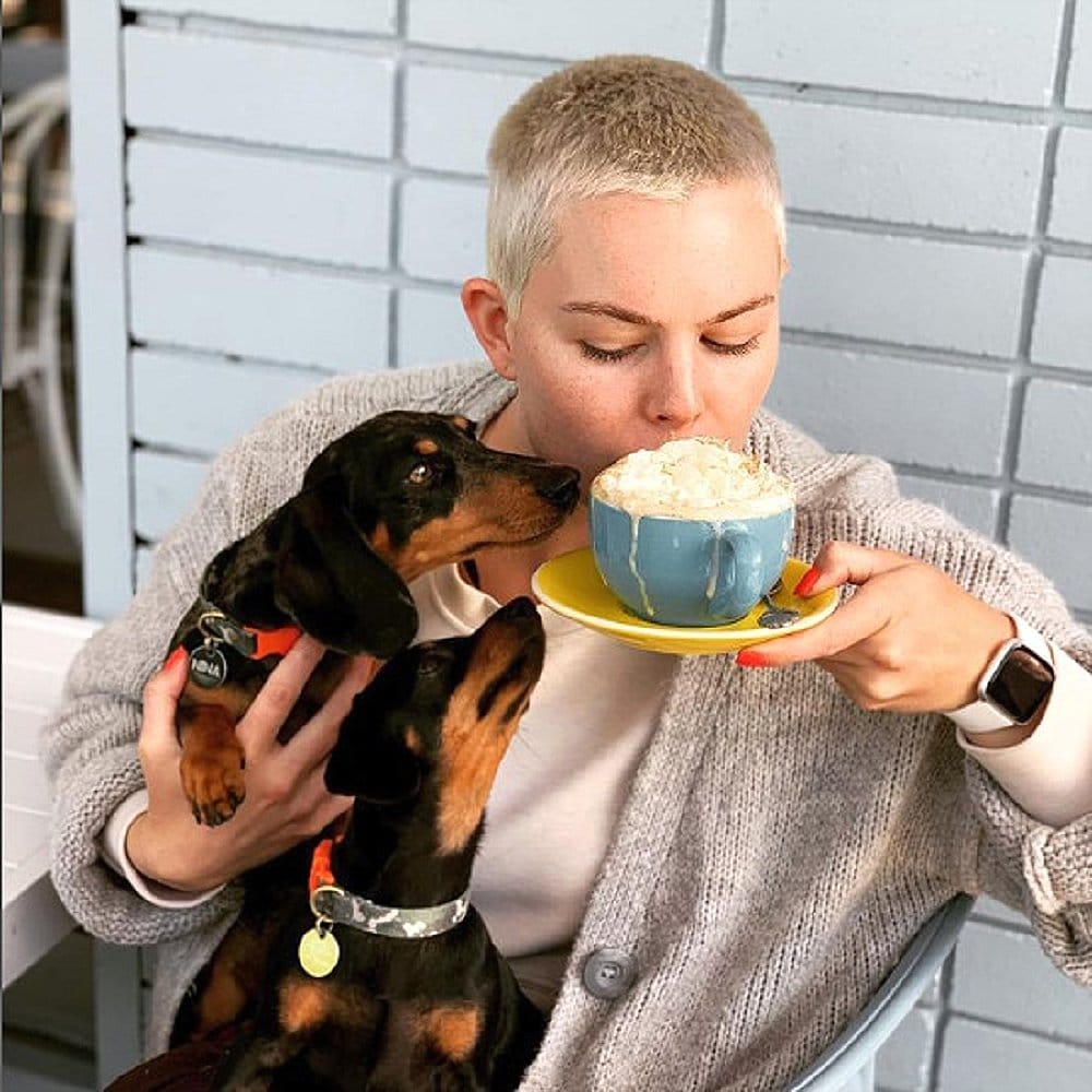 Woman sipping from a cup of coffee with her dog in her lap in a cafe called Little Oink in Canberra